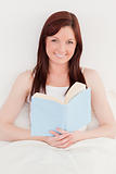 Good looking red-haired female reading a book while sitting on h