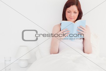 Attractive red-haired female reading a book while sitting on her