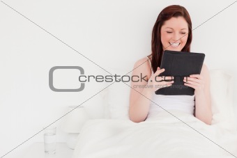 Attractive red-haired woman relaxing with her tablet while sitti