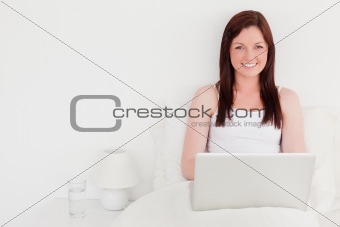 Attractive red-haired woman relaxing with her laptop while sitti