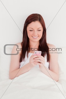 Beautiful red-haired woman writing a text on her mobile while si