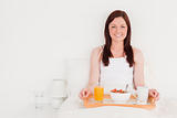 Attractive red-haired woman having her breakfast while sitting o