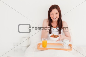 Pretty red-haired female having her breakfast while sitting on h