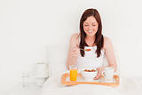 Beautiful red-haired female having her breakfast while sitting o