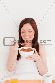 Attractive red-haired female having her breakfast while sitting 