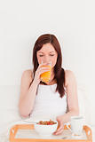 Attractive red-haired female drinking a glass of orange juice wh