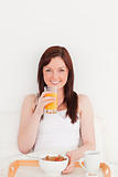 Pretty red-haired female drinking a glass of orange juice while 