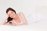 Attractive red-haired female relaxing with her mobile while lyin