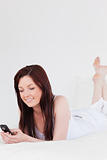 Pretty red-haired female writing a text on her mobile while lyin