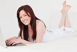 Pretty red-haired female relaxing with her laptop while lying on