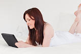 Attractive red-haired female relaxing with her tablet while lyin