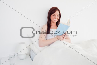 Good looking red-haired woman reading a book while sitting on he
