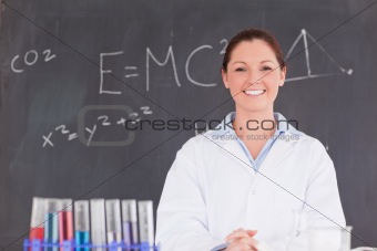 Cute scientist standing in front of a blackboard looking at the 