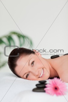 Portrait of a young woman with massage stones and a pink gerbera