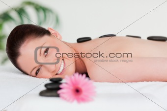 Happy young woman with a pink gerbera and massage stones