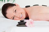Young woman receiving a black stone massage and a pink carnation