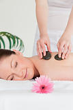 Happy young woman having a hot stone massage and a pink gerbera
