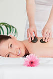 Smiling woman receiving a hot stone massage and a pink gerbera