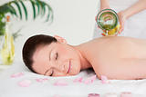 Masseuse pourring massage oil on a young woman's back in a spa