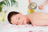 Masseuse versing massage oil on a beautiful woman's back in a sp