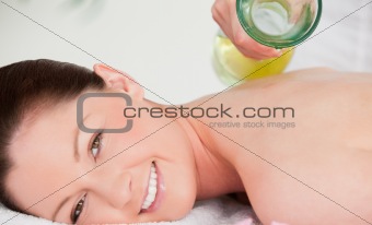 Masseuse pouring massage oil on a redhead woman's back