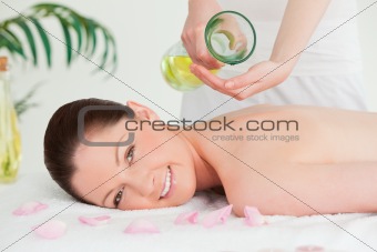 Smiling woman getting massage oil on a her back by a masseuse