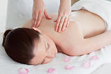 Cute redhead woman having a back massage surrounded by petals
