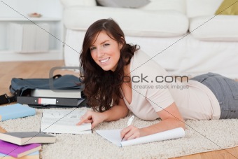 Young good looking female writing on a notebook while lying on a