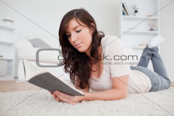 Young gorgeous woman reading a book while lying on a carpet