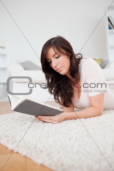 Young beautiful woman reading a book while lying on a carpet