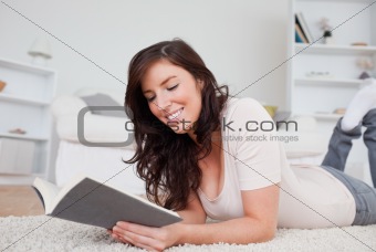 Young cute woman reading a book while lying on a carpet
