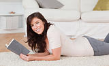 Young charming woman reading a book while lying on a carpet