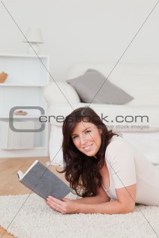 Young gorgeous female reading a book while lying on a carpet