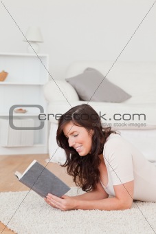 Young beautiful female reading a book while lying on a carpet