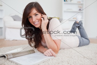 Young cute female reading a magazine while lying on a carpet