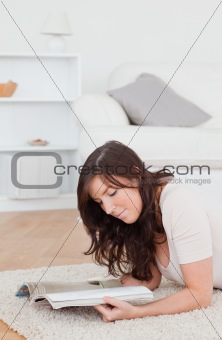 Young pretty woman reading a magazine while lying on a carpet