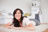 Good looking brunette female using headphones while lying on a c