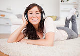 Smiling brunette female using headphones while lying on a carpet