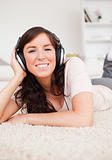 Charming brunette woman using headphones while lying on a carpet