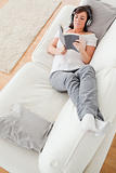 Young beautiful female reading a book while lying on a sofa