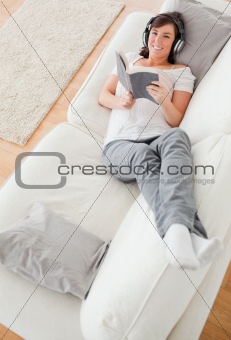 Young attractive female reading a book while lying on a sofa
