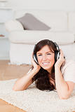 Gorgeous brunette woman using headphones while lying on a carpet
