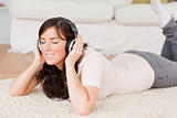 Cute brunette woman using headphones while lying on a carpet