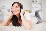 Smiling brunette woman using headphones while lying on a carpet