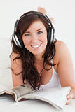 Gorgeous female with headphones reading a magazine while lying