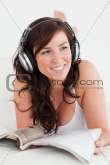 Cute female with headphones reading a magazine while lying