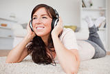 Cheerful brunette woman using headphones while lying on a carpet