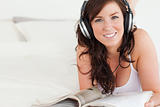 Good looking female with headphones reading a magazine while lyi