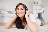 Glad brunette woman using headphones while lying on a carpet