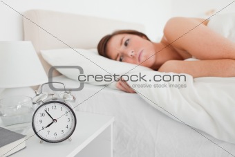 Lovely brunette woman awaking with a clock while lying